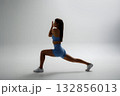 Woman performs a lunging exercise in a minimalistic studio, showcasing strength and focus during a workout session 132856013