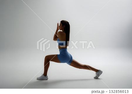 Woman performs a lunging exercise in a minimalistic studio, showcasing strength and focus during a workout session 132856013