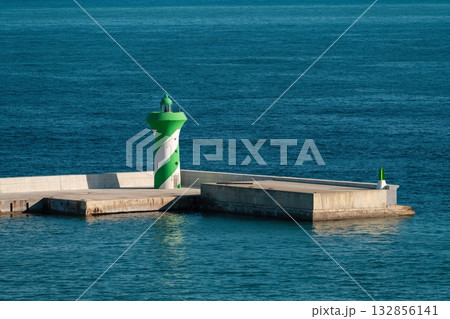 Green lighthouse with a white spiral stripe stands on a concrete breakwater in the port Green lighthouse with a white spiral stripe stands on a concrete breakwater in the port 132856141