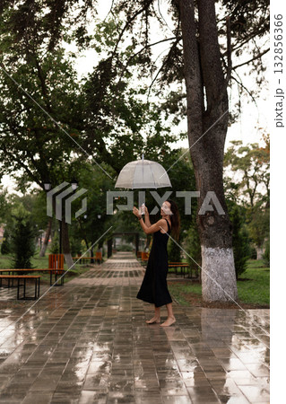 Woman umbrella rain, joyful barefoot woman enjoying a refreshing walk in a wet park. Woman umbrella rain, joyful barefoot woman enjoying a refreshing walk in a wet park. 132856366