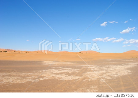 A desert landscape with a blue sky and footprints in the sand A desert landscape with a blue sky and footprints in the sand 132857516