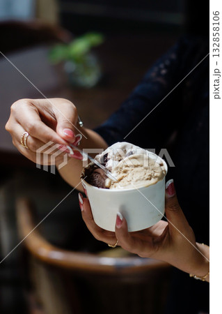 Close-up of hands holding and scooping ice cream in a cup at a cozy cafe 132858106