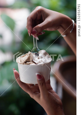 Close up of hands holding a cup of creamy gelato ice cream with spoon in natural light outdoor cafe setting, showing melting texture and elegant manicure for summer dessert and lifestyle concept Close up of hands holding a cup of creamy gelato ice cream with spoon in natural light outdoor cafe setting, showing melting texture and elegant manicure for summer dessert and lifestyle concept 132858791