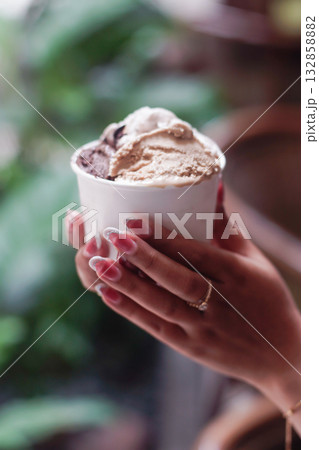 Close up of hands holding a cup of creamy gelato ice cream in natural light outdoor cafe setting, showing melting texture and elegant manicure for summer dessert and lifestyle concept Close up of hands holding a cup of creamy gelato ice cream in natural light outdoor cafe setting, showing melting texture and elegant manicure for summer dessert and lifestyle concept 132858882