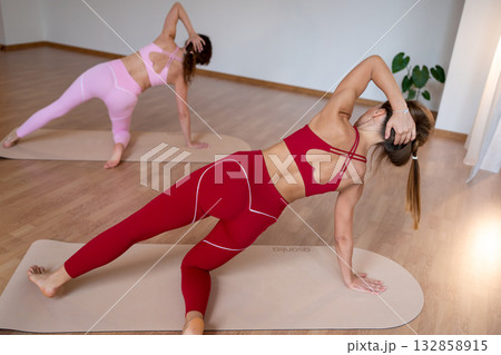 Active women execute coordinated side planks with trainer guidance in welllit studio setting Active women execute coordinated side planks with trainer guidance in welllit studio setting 132858915