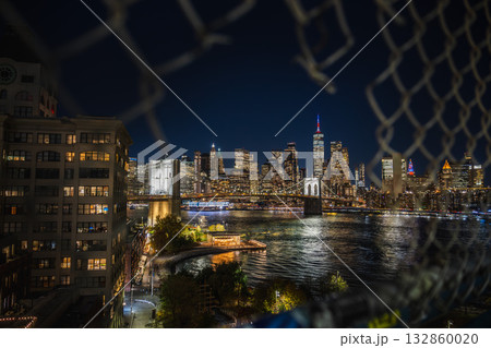 Night view of Manhattan skyline and Brooklyn Bridge through a hole in the Manhattan Bridge fence Night view of Manhattan skyline and Brooklyn Bridge through a hole in the Manhattan Bridge fence 132860020