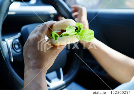 Asian woman driver hold and eat hamburger food in car. 132860254