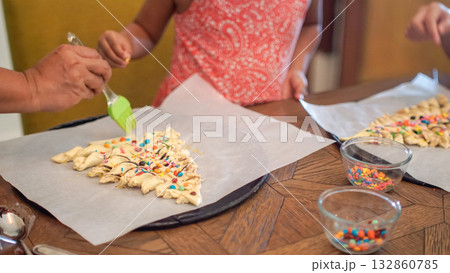 Family decorating Christmas tree-shaped pastry with colorful toppings and egg wash during a festive baking activity. Perfect for holiday, parenting, and family lifestyle concepts. 132860785