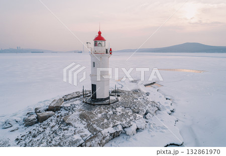 On an icy island in Vladivostok, a lighthouse stands surrounded by frozen water, with the dawn casting a calming glow. 132861970