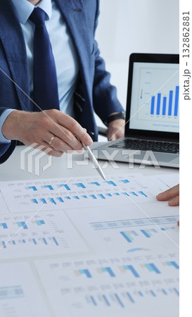 Businesspeople sitting at the table and pointing into financial charts while discussing financial data, market trends during meeting in modern office. Business people concept 132862881