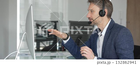 Male call center agent wearing a headset, providing online customer support and consulting clients during a video call. Business communication concept 132862941