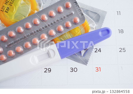Pregnancy test with birth control pills and condom for female on calendar, ovulation day. 132864558