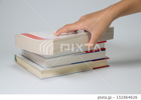 積まれた本から一冊を取る手元 132864626