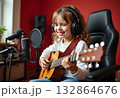 A girl with headphones and a guitar sits at the microphone in a recording studio 132864676
