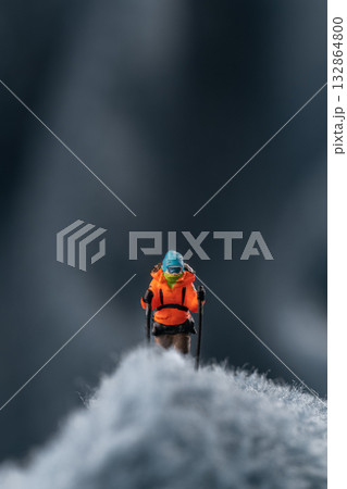 A miniature mountain climber figurine on a fuzzy fleece lining resembling a snow-covered surface, with a blurred background of a mountain or ice wall A miniature mountain climber figurine on a fuzzy fleece lining resembling a snow-covered surface, with a blurred background of a mountain or ice wall 132864800