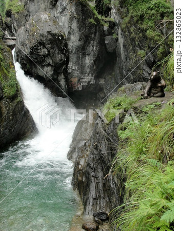 A  stream of clear water, a waterfall flows down from high mountains down over rocks between high mountains 132865023