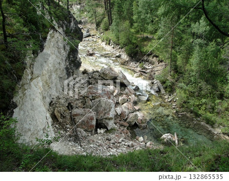 A turbulent stream of clear water, a waterfall flows down from high mountains down over rocks between high mountains A turbulent stream of clear water, a waterfall flows down from high mountains down over rocks between high mountains 132865535