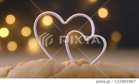 Two heart-shaped metal cookie cutters placed on raw dough, with warm bokeh lights in the background suggesting romance or holidays. Two heart-shaped metal cookie cutters placed on raw dough, with warm bokeh lights in the background suggesting romance or holidays. 132865967