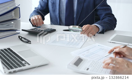 Male financial analysts with female colleague examining documents, using magnifying glass and calculator at workplace in office. Audit and taxes in business 132866214