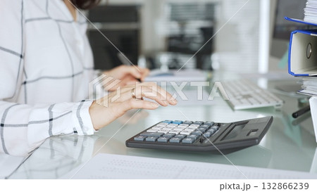 Woman calculating finances with black calculator, managing taxes, invoices, and accounting documents in office. Audit and taxes in business 132866239