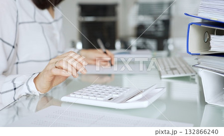 Woman working in office, calculating finances with white calculator, managing accounting paperwork and business expenses. Audit and taxes in business 132866240