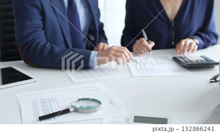 Magnifying glass and calculator over financial documents opposite financial team of male and female auditors, reviewing reports, collaborating on accounting details in office. Audit and taxes 132866241