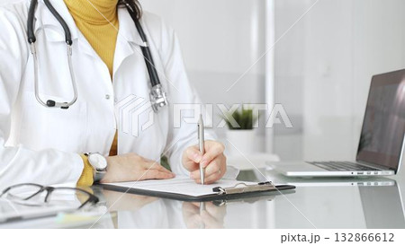 Female physician or medic completing paperwork, preparing a diagnosis, or providing healthcare service in a clean modern office. Medicine, healthcare and science concept Female physician or medic completing paperwork, preparing a diagnosis, or providing healthcare service in a clean modern office. Medicine, healthcare and science concept 132866612