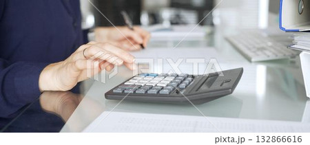 Woman calculating finances on a desk in a modern office, working on accounting, banking, and budget planning. Audit and taxes in business Woman calculating finances on a desk in a modern office, working on accounting, banking, and budget planning. Audit and taxes in business 132866616