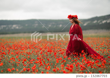 Woman poppy field walking through a beautiful blooming landscape wearing an elegant red dress Woman poppy field walking through a beautiful blooming landscape wearing an elegant red dress 132867703