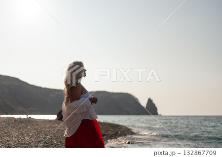 Woman, beach, sunset. Blond woman on pebbly beach looking at ocean during serene golden hour with copy space. Woman, beach, sunset. Blond woman on pebbly beach looking at ocean during serene golden hour with copy space. 132867709