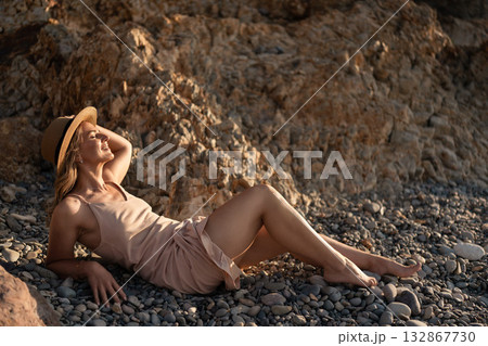Woman beach summer vacation. Happy young woman relaxing on pebble beach enjoying warm sunlight by rocky cliff. Woman beach summer vacation. Happy young woman relaxing on pebble beach enjoying warm sunlight by rocky cliff. 132867730