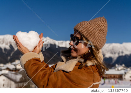Snow Heart Mountains Winter: Woman holding snow heart, sunny Alps mountains, winter vacation joy. 132867740