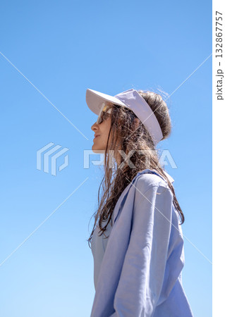 Woman Visor Sky. Young woman in visor and sunglasses outdoors under clear blue sky for sun protection. Woman Visor Sky. Young woman in visor and sunglasses outdoors under clear blue sky for sun protection. 132867757