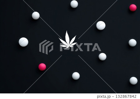 Colorful pills create patterns against a black surface with a central cannabis leaf design 132867842