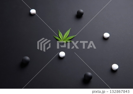 Unique arrangement of pills and cannabis leaves on a dark surface in an artistic display Unique arrangement of pills and cannabis leaves on a dark surface in an artistic display 132867843