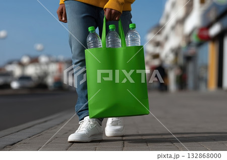 Person carrying a green bag filled with empty plastic bottles while walking on the street 132868000