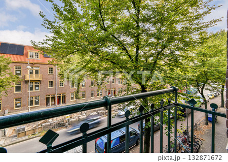 A vibrant urban scene seen from a balcony, showcasing lush green trees against a backdrop of colorful buildings and parked bicycles. A sunny day adds to the charm. 132871672