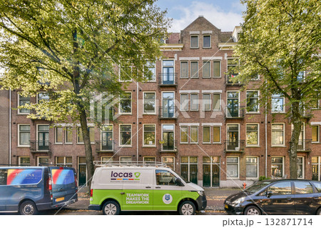 A picturesque urban landscape showcasing a charming building adorned with large windows, framed by vibrant trees and parked vehicles, capturing suburban tranquility. A picturesque urban landscape showcasing a charming building adorned with large windows, framed by vibrant trees and parked vehicles, capturing suburban tranquility. 132871714