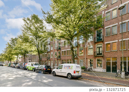 A picturesque street scene featuring lined buildings with trees, parked cars, and a sunny blue sky, embodying urban tranquility. 132871725