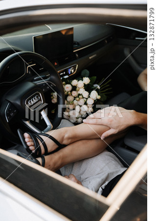 Romantic engagement couple in car with bouquet and gentle touch on legs Romantic engagement couple in car with bouquet and gentle touch on legs 132871799