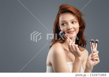 Beauty And Makeup. Red-Haired Girl Posing Holding Cosmetic Brushes Looking Aside Over White Background. Make-Up Advertisement Banner. Studio Shot, Panorama With Copy Space 132871968
