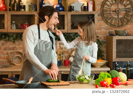 Happy Young Family Father And Daughter Having Fun While Cooking In Kitchen Together, Little Girl Feeding Dad With Vegetables While Preparing Healthy Food At Home, Making Lunch Or Dinner, Free Space Happy Young Family Father And Daughter Having Fun While Cooking In Kitchen Together, Little Girl Feeding Dad With Vegetables While Preparing Healthy Food At Home, Making Lunch Or Dinner, Free Space 132872002
