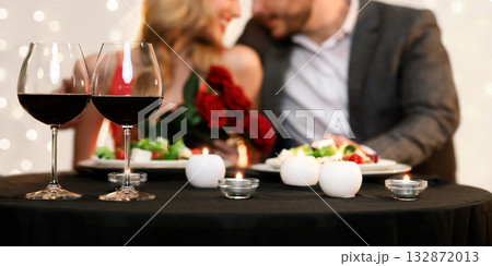 Valentine's Day Dinner Concept. Two Glasses With Red Wine On Table, Romantic Couple Blurred In Background Valentine's Day Dinner Concept. Two Glasses With Red Wine On Table, Romantic Couple Blurred In Background 132872013