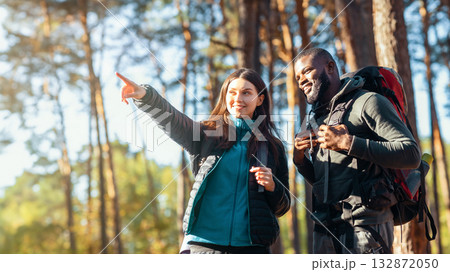 Mixed race couple of hikers walking by forest, girl pointing somewhere, sun flare Mixed race couple of hikers walking by forest, girl pointing somewhere, sun flare 132872050