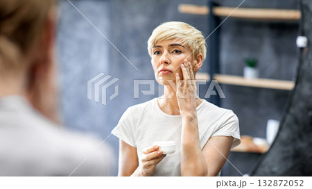 Facial Cream. Lady Applying Moisturizer Looking At Reflection In Mirror Standing In Bathroom At Home. Selective Focus 132872052