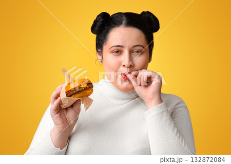 Young obese girl eating burger and licking fingers, enjoying fast food, high calorie nutrition 132872084