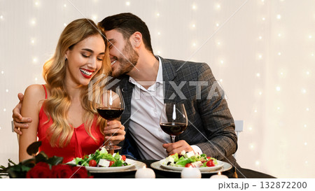 Loving Pair Dining In Restaurant, Having Romantic Date, Celebrating Valentine's Day Together. Man Whispering Into Girlfriend's Ear, Copy Space Loving Pair Dining In Restaurant, Having Romantic Date, Celebrating Valentine's Day Together. Man Whispering Into Girlfriend's Ear, Copy Space 132872200