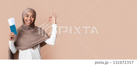 Time To Travel. Joyful afro islamic woman in hijab holding passport and tickets, gesturing ok sign over yellow background with empty space Time To Travel. Joyful afro islamic woman in hijab holding passport and tickets, gesturing ok sign over yellow background with empty space 132872357