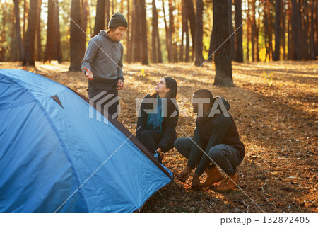 Cheerful multiracial backpackers setting camp in autumn forest, sun flare, free space 132872405