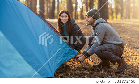 Active couple settle blue camping tent in the middle of autumn forest, having fun, copy space 132872459